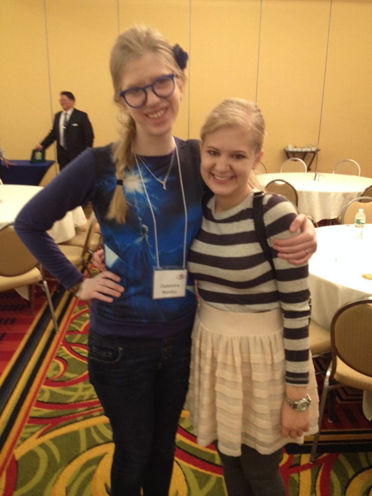 casey and cassandra pose in a hotel conference room, smiling and with one hand on their hips, march 2015