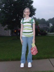 cassandra standing outside for her first day of 7th grade wearing chunky white skater sneakers, light wash bootcut jeans, and a striped green polo