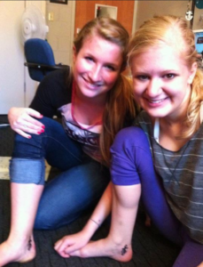 Casey and her best friend Audrey after getting their matching tattoos. Casey and Audrey pose sitting on the ground and propping their knee up so you can see both girls with their tattoos