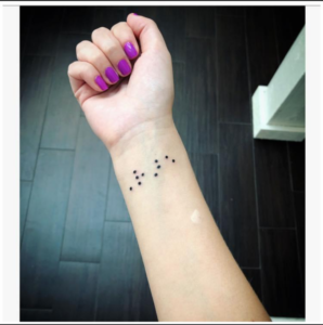 Caseys second tattoo on her right wrist. photo shows the inside of her wrist and pink nails with the word "rare" tattooed in Braille