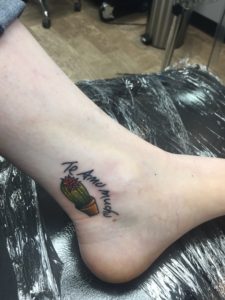 Cassandras ankle with her second tattoo, a small, round, potted cactus in full color with a pink flower on top. words in handwriting arc on the left side of it that read "te amo mucho," or "i love you a lot" in Spanish