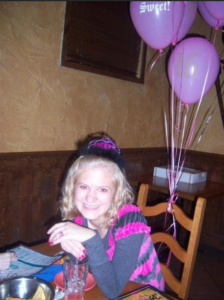 16 year old casey smiling at a table with pink balloons and a pink tiara on her 16th birthday