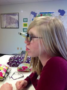 side profile of cassandra in high school with long blonde hair and her bioptic lenses which are glasses with a rectangular monocular mounted on