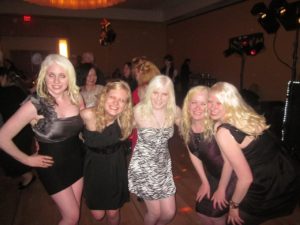 casey surrounded by four other women with albinism in cocktail dresses. they all pose together, and casey grins from ear to ear