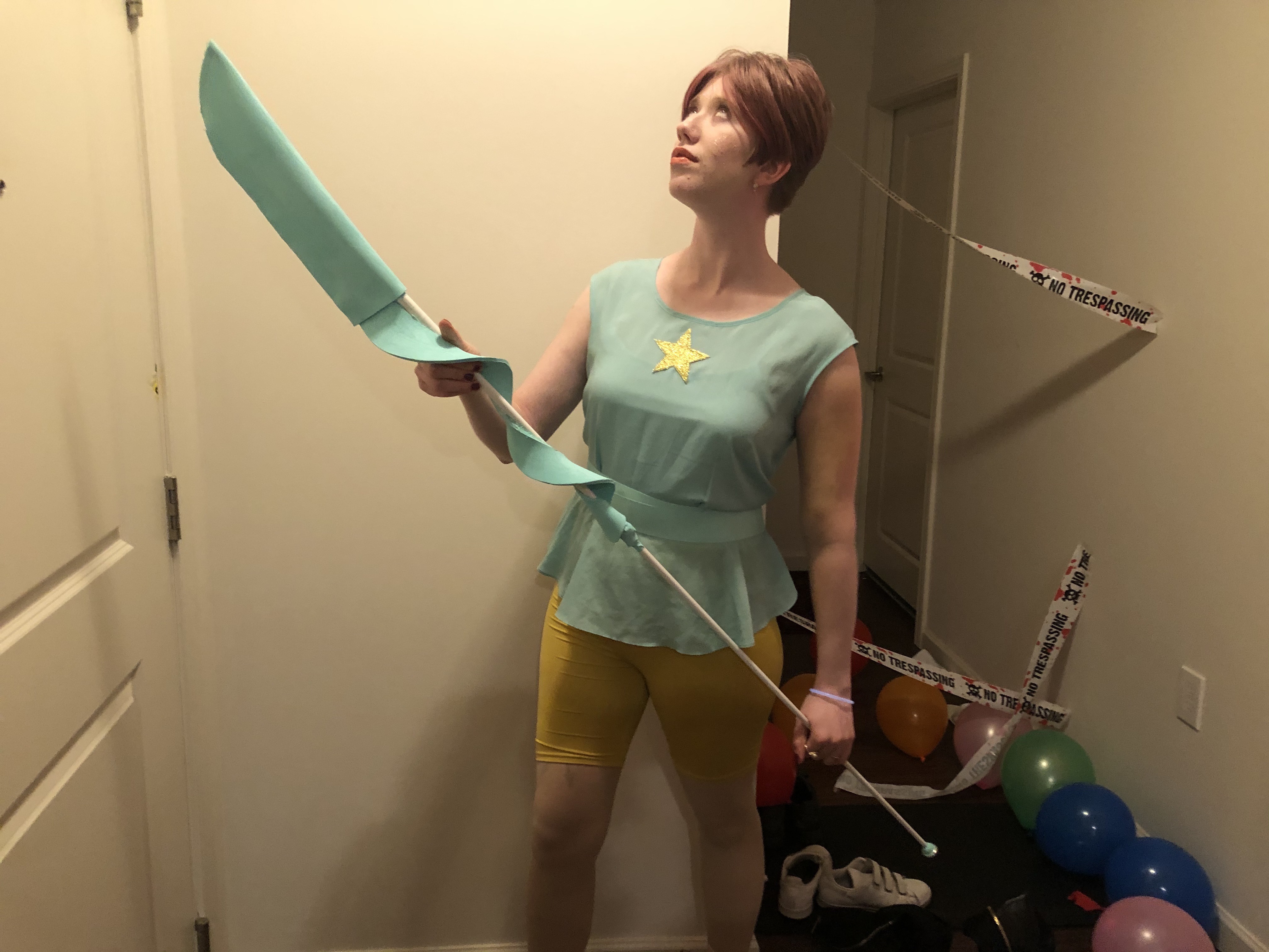 cass as pearl from steven universe. she wears a mint green to with a star, a ribbon belt, and yellow compression shorts. she holds pearl's spear and looks to the top left