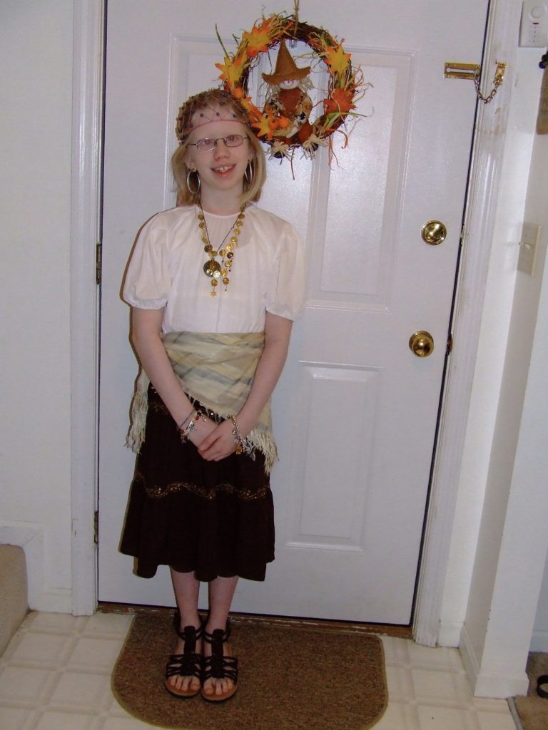 cassandra dressed as a gypsy. she wears a long skirt with a wrap, white loose top, and long costume jewelry necklaces