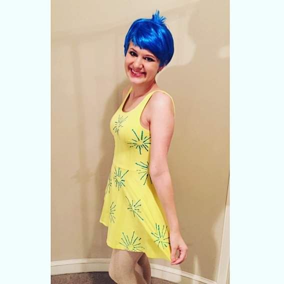 case dressed as joy from inside out. she wears a yellow skater dress and a blue pixie cut wig