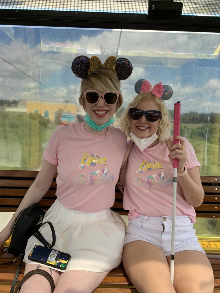 picture of case and cass in disney! they wear matching light pink tops with pastel print that says epcot. cass wears a white miniskirt and case wears white shorts, and both smile while sitting in the skyliner cable car