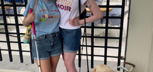 casey and cassandra posing together in the summertime. they both wear national organization for albinism & hypopigmentation shirts and mickey ears and stand outside smiling. they each wear a pair of crocs