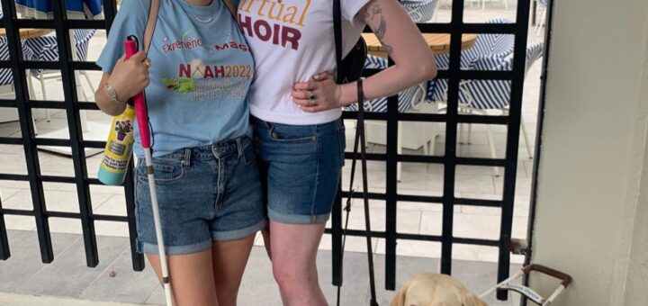 casey and cassandra posing together in the summertime. they both wear national organization for albinism & hypopigmentation shirts and mickey ears and stand outside smiling. they each wear a pair of crocs