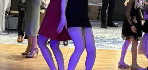 case and cass stand back to back in their party dresses, laughing and singing as they dance on a colorfully lit dance floor