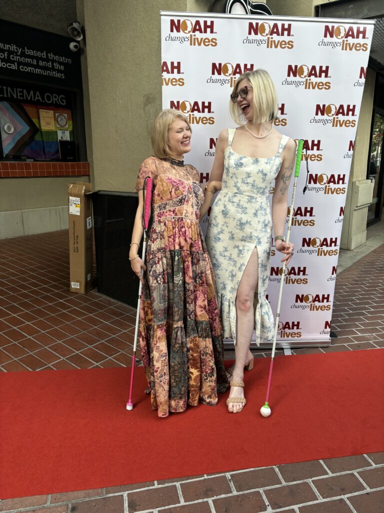 case and cass stand outside on a small red carpet. dressed in long formal dresses, they look at each other while laughing and hold their canes.