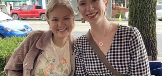 Case and Cass sit smiling close together at an outdoor table in front of a street lined with shops