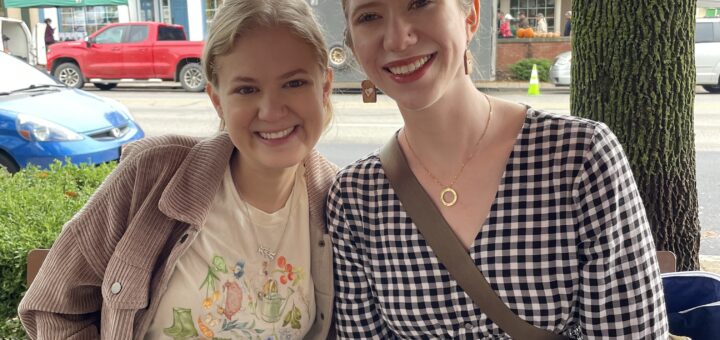 Case and Cass sit smiling close together at an outdoor table in front of a street lined with shops