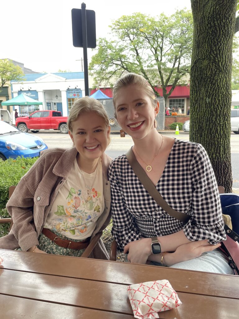 Case and Cass sit smiling close together at an outdoor table in front of a street lined with shops