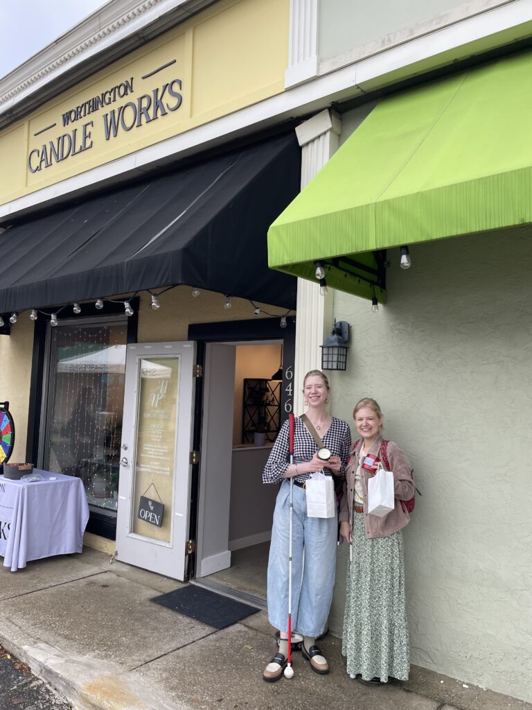 Case & Cass smile outside Worthington Candle Works, standing beside the shop’s open doorway holding candles in jars and white shopping bags