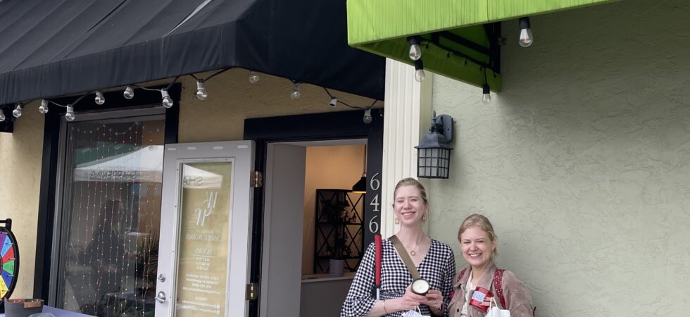 Case & Cass smile outside Worthington Candle Works, standing beside the shop’s open doorway holding candles in jars and white shopping bags