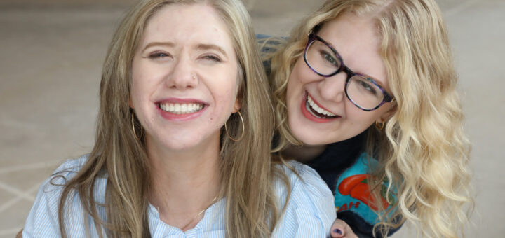 Cass and Case smile and laugh together for the camera. Cass wears a blue-and-white striped shirt with a bow, while Case wears glasses and a colorful shirt.